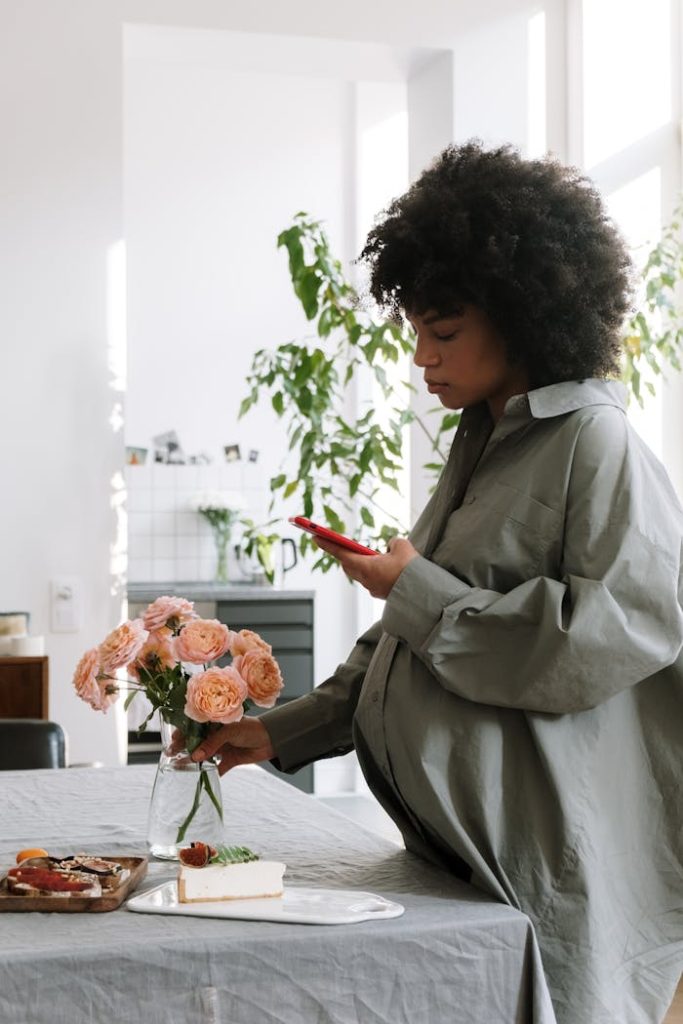 pexels-photo-5857828 Expectant mother enjoying flowers and cake in a sunlit room.